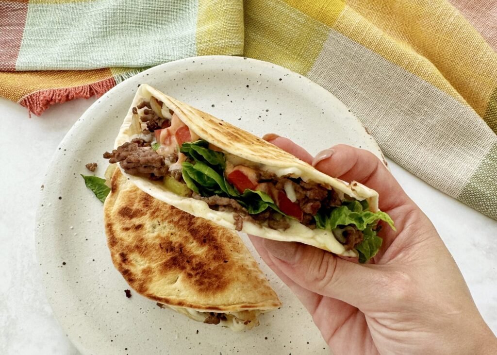Close-up of Cheesy Beef Tacos filled with seasoned beef, melted cheese, lettuce, tomato, and drizzled with sriracha mayo.