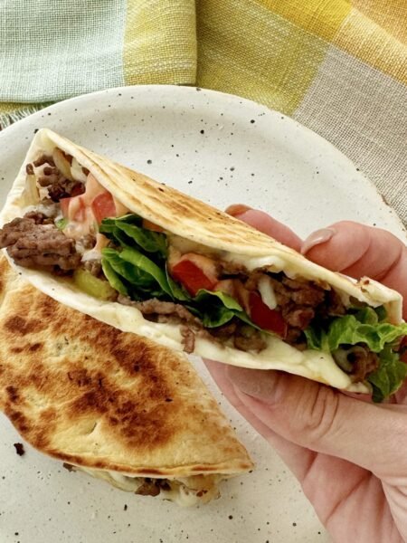 Close-up of Cheesy Beef Tacos filled with seasoned beef, melted cheese, lettuce, tomato, and drizzled with sriracha mayo.