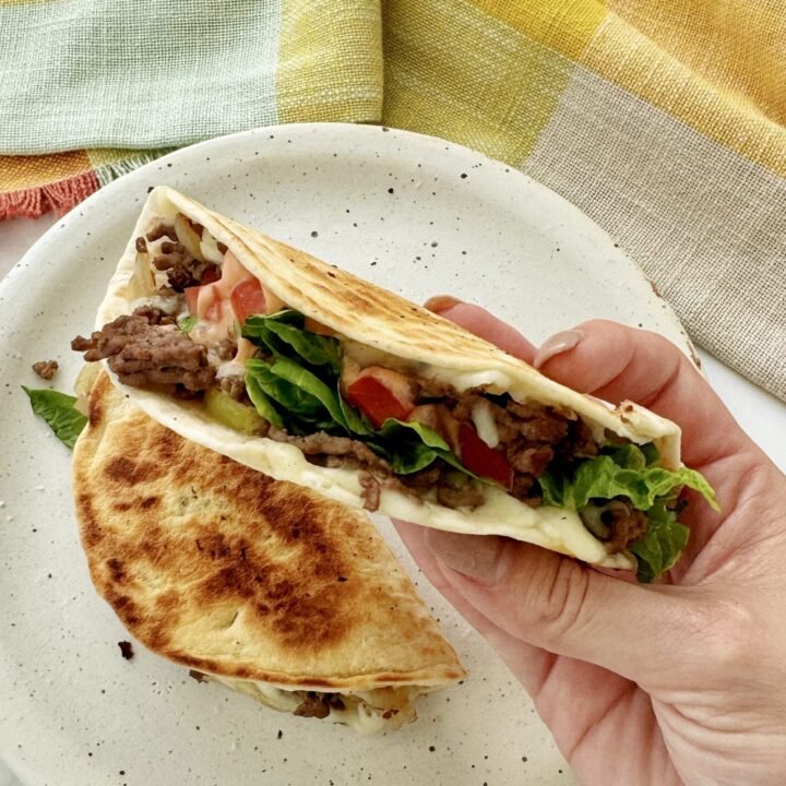 Close-up of Cheesy Beef Tacos filled with seasoned beef, melted cheese, lettuce, tomato, and drizzled with sriracha mayo.