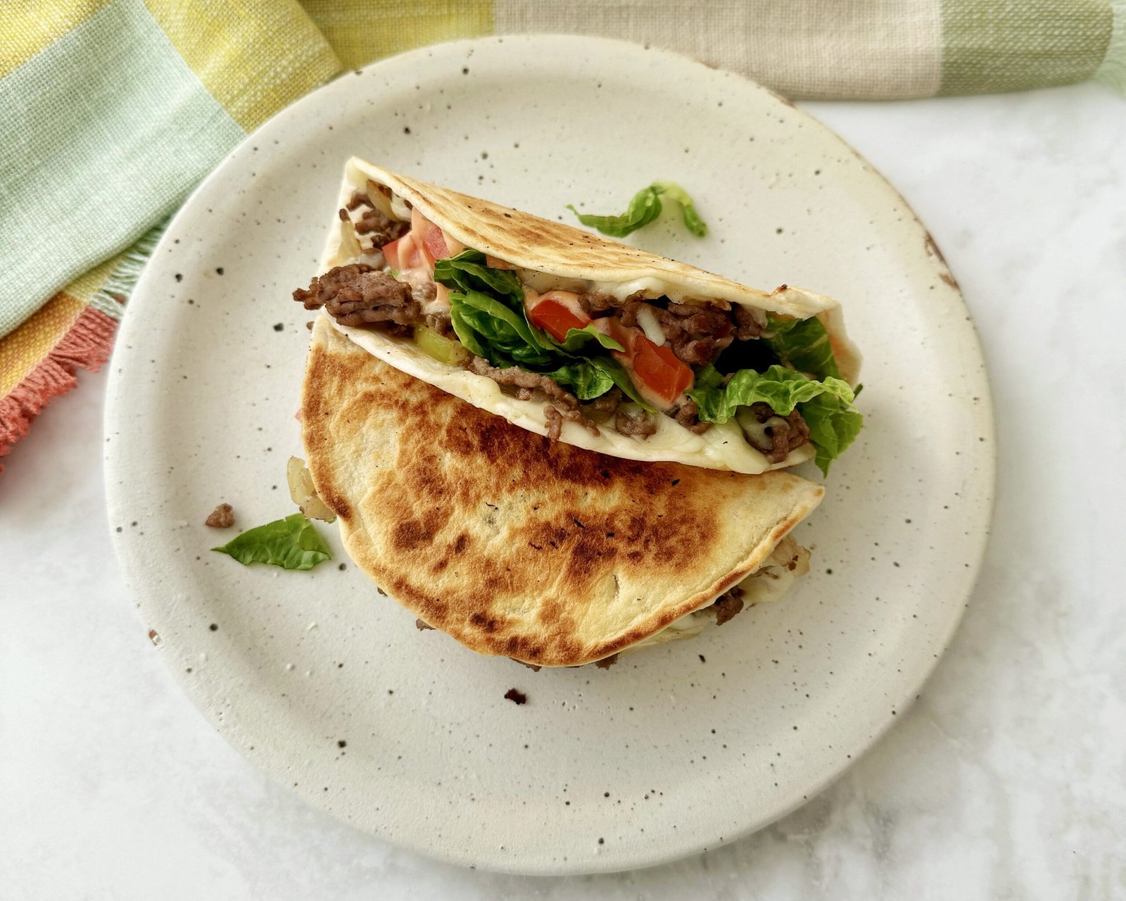 Close-up of Cheesy Beef Tacos filled with seasoned beef, melted cheese, lettuce, tomato, and drizzled with sriracha mayo.