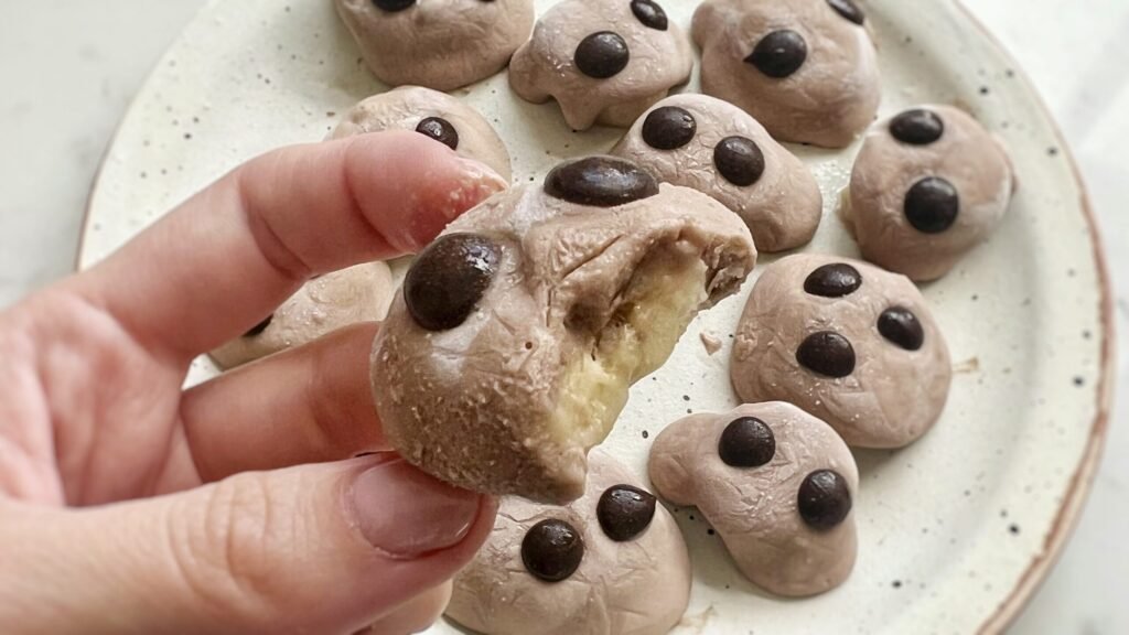 Chocolate banana protein bites topped with yogurt and chocolate chips on a parchment-lined tray