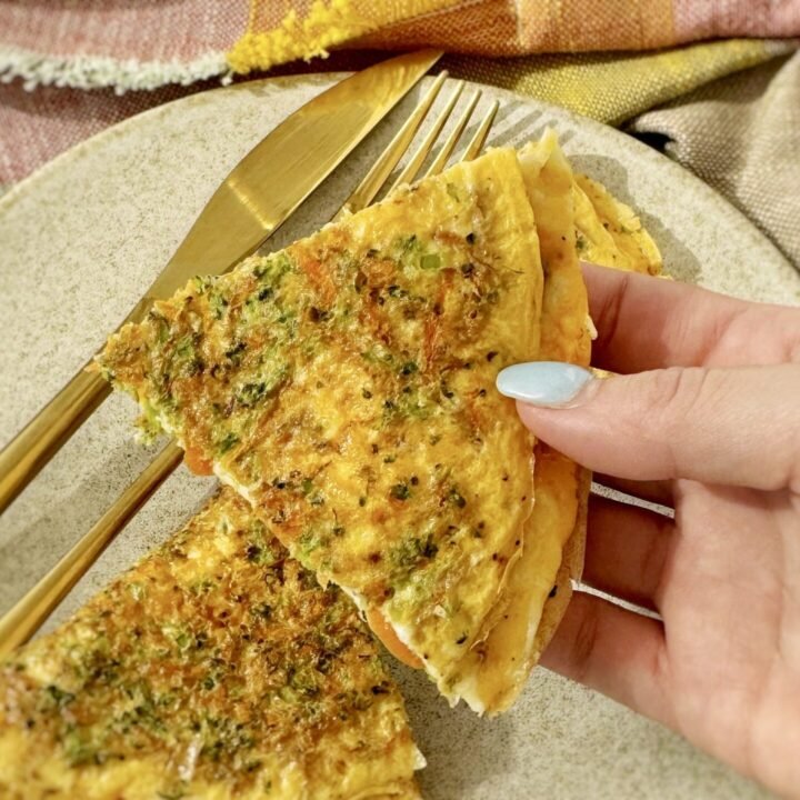 A golden omelette with crisp edges, filled with grated carrots, broccoli, and melted mozzarella, served hot on a white plate with a fresh herb garnish.