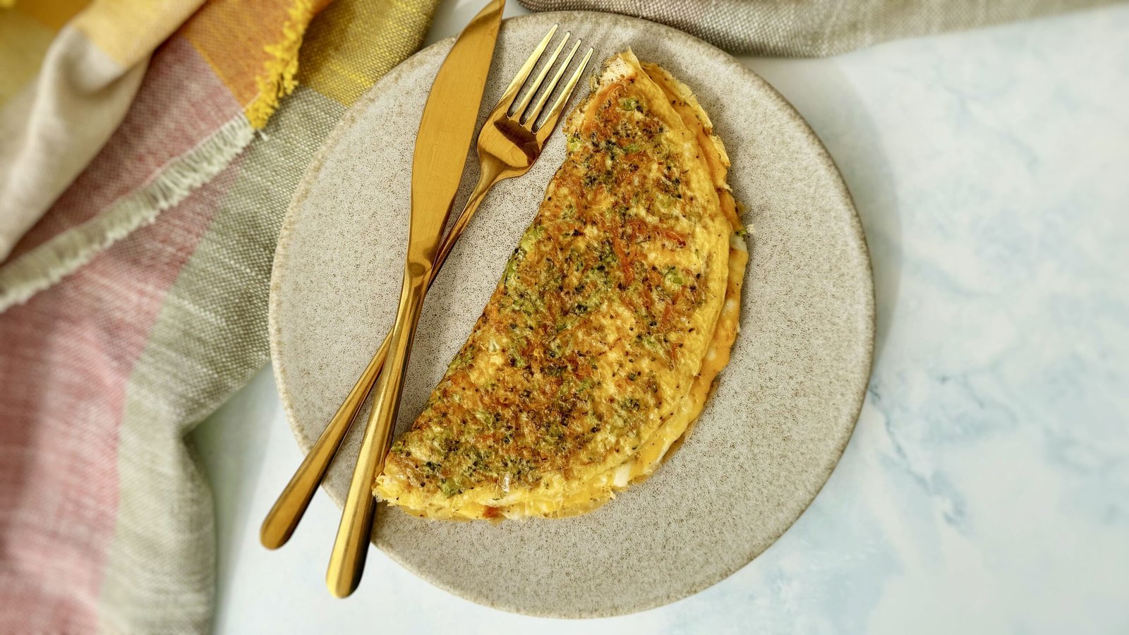 A golden omelette with crisp edges, filled with grated carrots, broccoli, and melted mozzarella, served hot on a white plate with a fresh herb garnish.