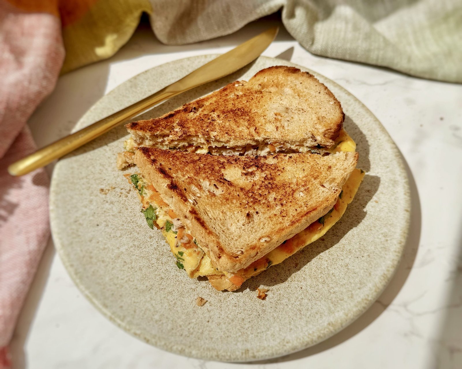 Crispy egg sandwich folded with tuna, grated carrot, parsley, and Parmesan between slices of toasted wholemeal bread on a plate.
