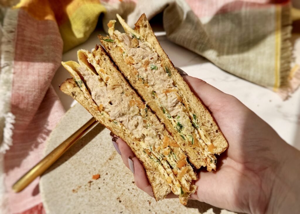Crispy egg sandwich folded with tuna, grated carrot, parsley, and Parmesan between slices of toasted wholemeal bread on a plate.