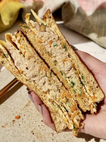 Crispy egg sandwich folded with tuna, grated carrot, parsley, and Parmesan between slices of toasted wholemeal bread on a plate.