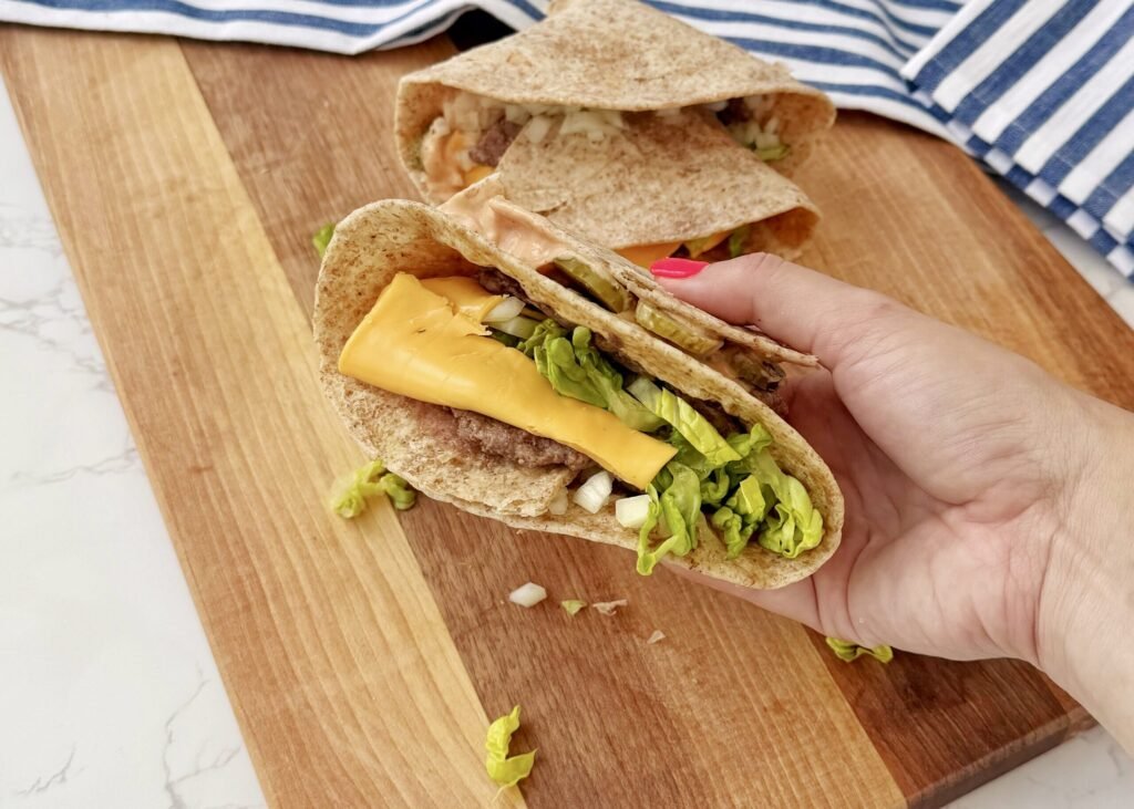 a hand holding a tortilla with meat and cheese. Big Mac Smash Wrap