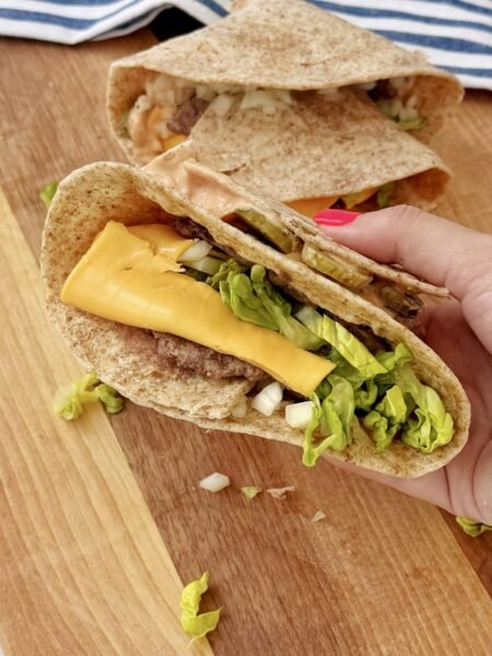 a hand holding a tortilla with meat and cheese. Big Mac Smash Wrap