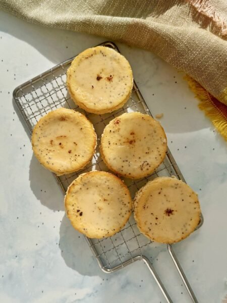 Mini Lemon and Poppyseed Cottage Cheesecakes served in paper liners, topped with lemon zest and fresh berries on a white plate