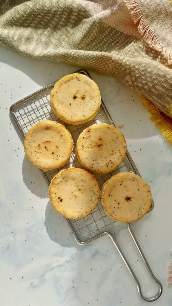 Mini Lemon and Poppyseed Cottage Cheesecakes served in paper liners, topped with lemon zest and fresh berries on a white plate