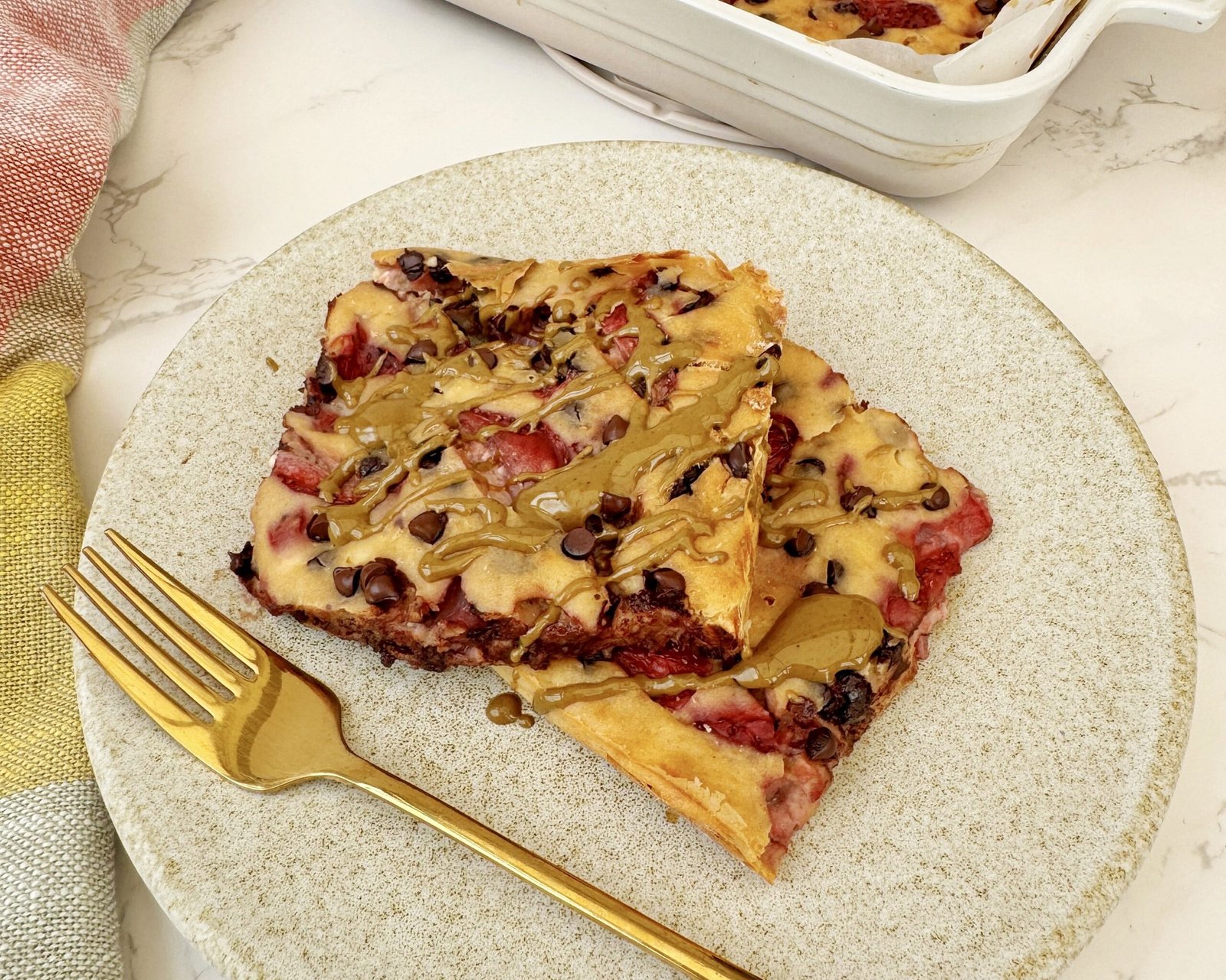 aked strawberry and dark chocolate pancakes in a tray, sliced and drizzled with pistachio butter.