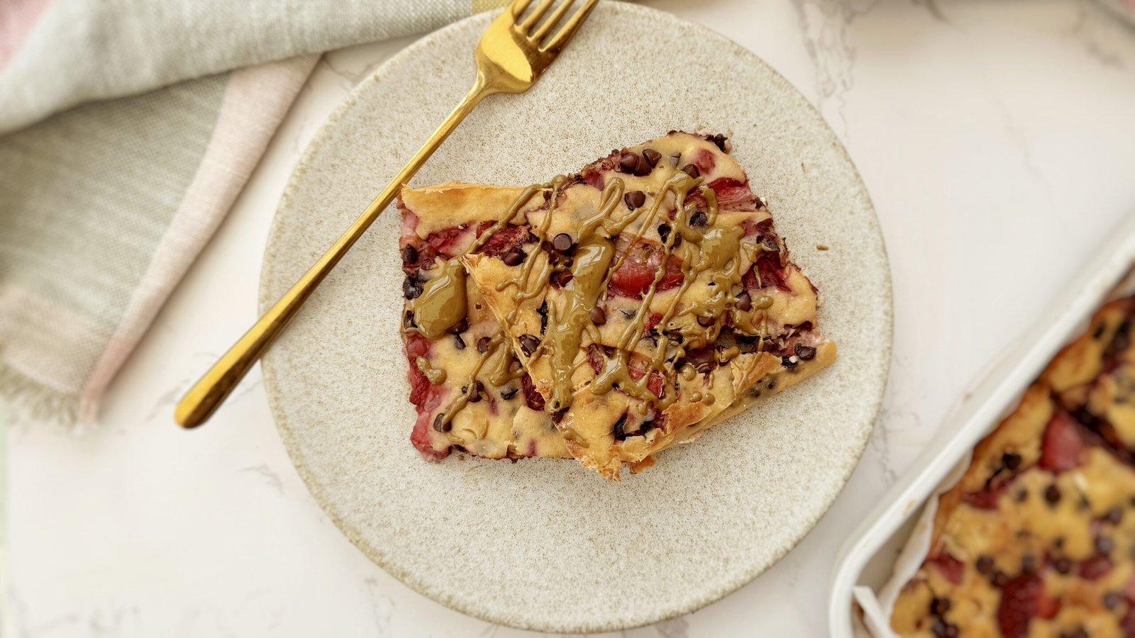 aked strawberry and dark chocolate pancakes in a tray, sliced and drizzled with pistachio butter.
