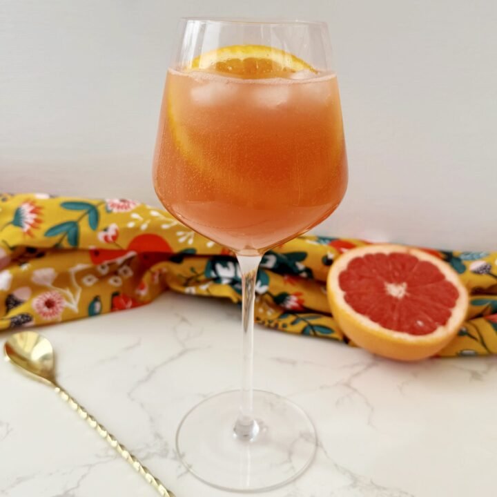 A vibrant Aperol Spritz-Inspired Mocktail in a wine glass, filled with ice, orange slice garnish, and a fizzy orange-pink hue — perfect for summer parties and alcohol-free toasts.