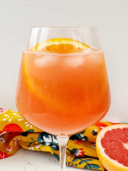 A vibrant Aperol Spritz-Inspired Mocktail in a wine glass, filled with ice, orange slice garnish, and a fizzy orange-pink hue — perfect for summer parties and alcohol-free toasts.
