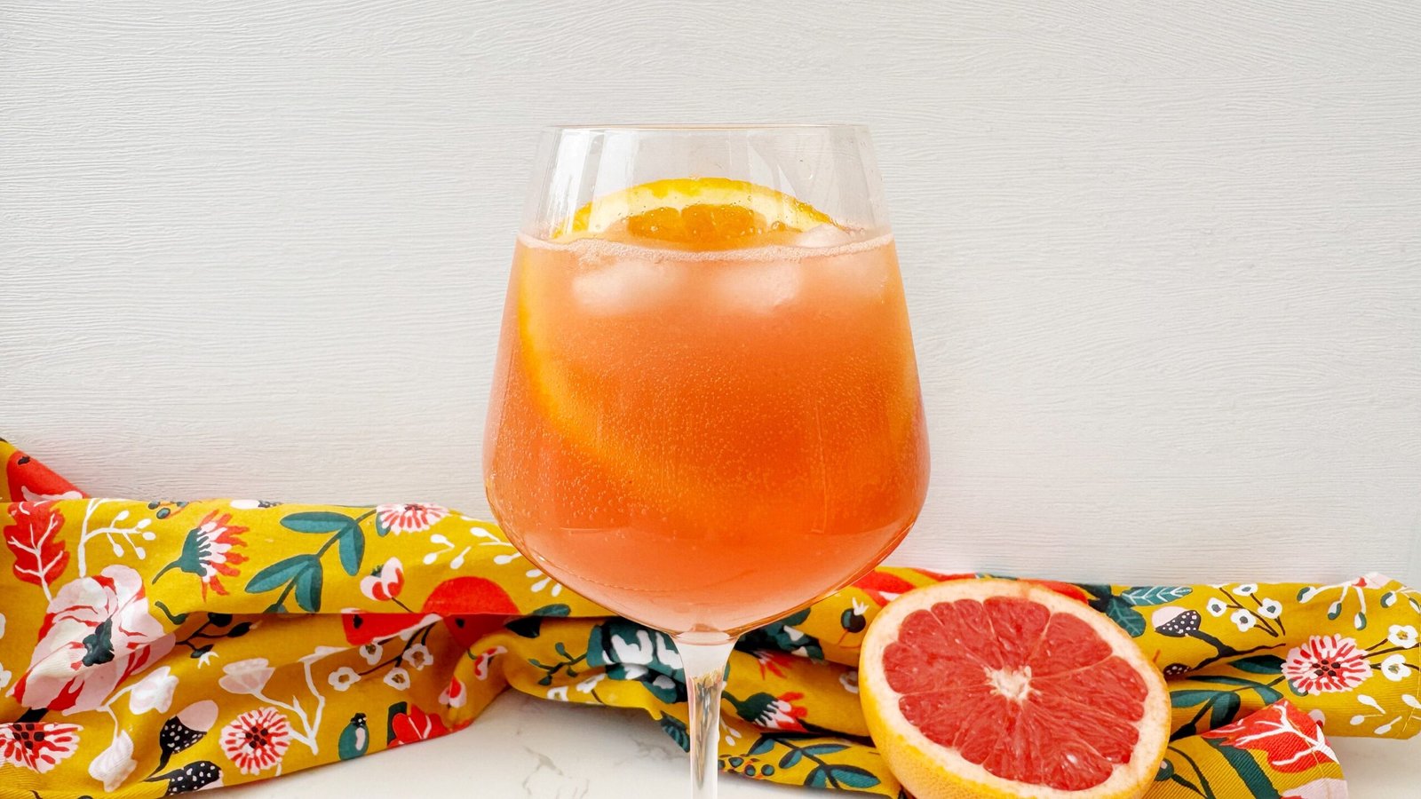 A vibrant Aperol Spritz-Inspired Mocktail in a wine glass, filled with ice, orange slice garnish, and a fizzy orange-pink hue — perfect for summer parties and alcohol-free toasts.