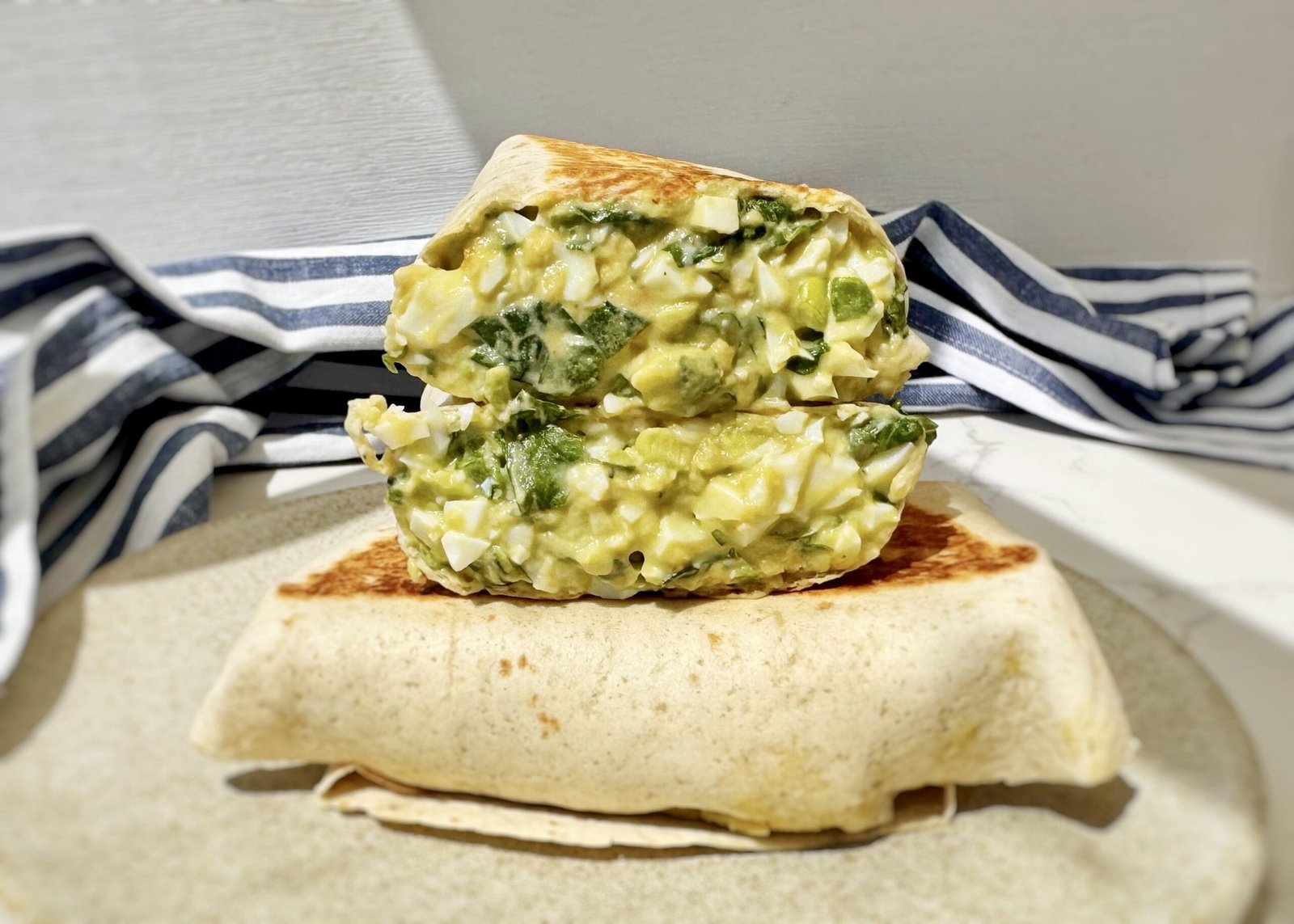 Toasted chopped egg salad wrap filled with avocado, Skyr, spinach and mustard on a wooden board