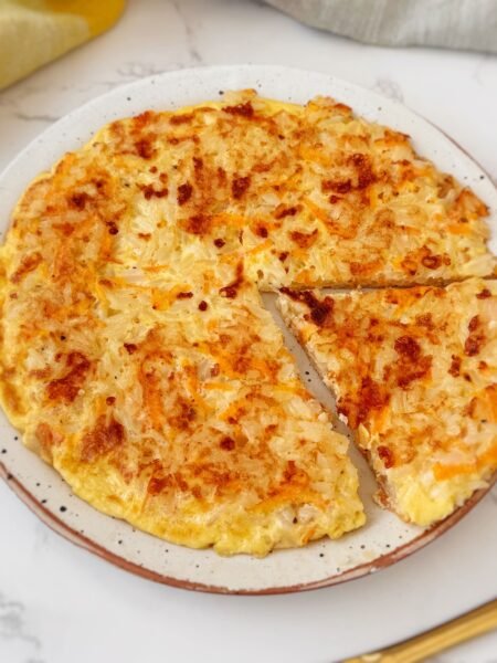 A golden-brown Crispy Rice and Carrot Pie sliced into wedges on a plate, with visible flecks of carrot and melted cheese.