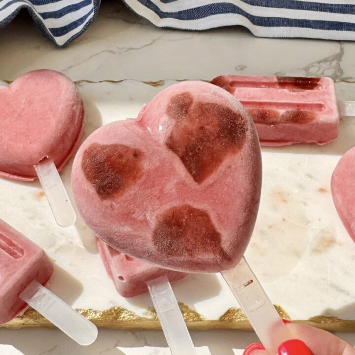 Close-up of vibrant pink raspberry protein ice lollies with visible berry jam swirls, served on a chilled platter with fresh raspberries and mint leaves.