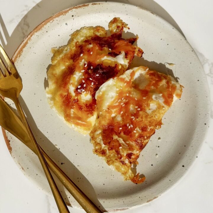 Hot Honey Crispy Carrot Eggs in a non-stick pan with runny yolks, golden mozzarella crust, grated carrots, and sesame seeds – a spicy, high-protein vegetarian breakfast perfect for quick UK brunch recipes.