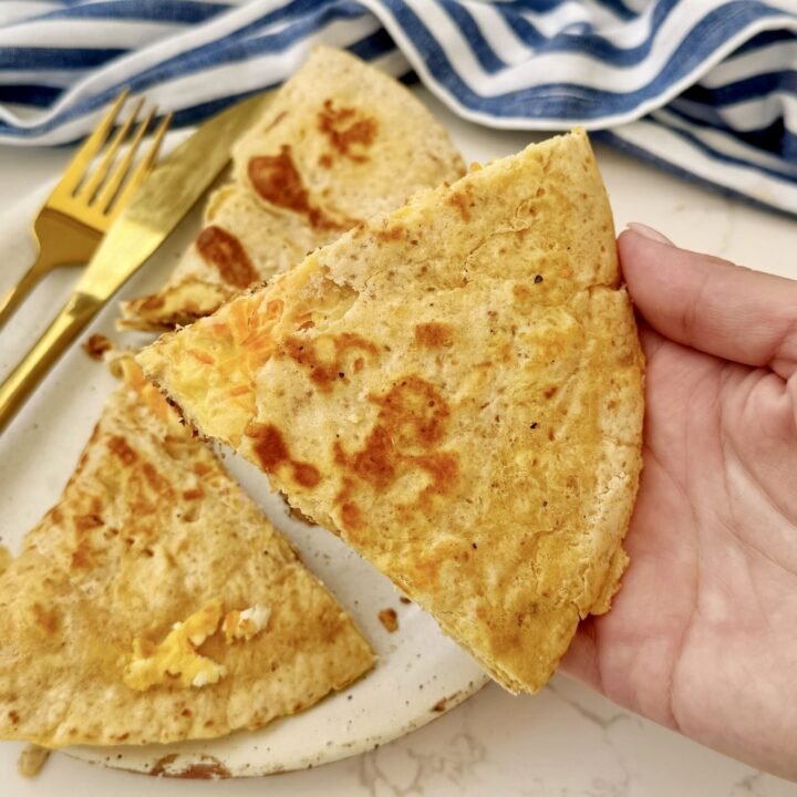 A folded tortilla omelette with a golden, crispy crust, showing melted feta, grated carrot, and fluffy egg layers. Served on a plate with fresh greens and lemon wedges.