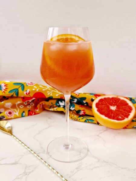 A vibrant Aperol Spritz-Inspired Mocktail in a wine glass, filled with ice, orange slice garnish, and a fizzy orange-pink hue — perfect for summer parties and alcohol-free toasts.