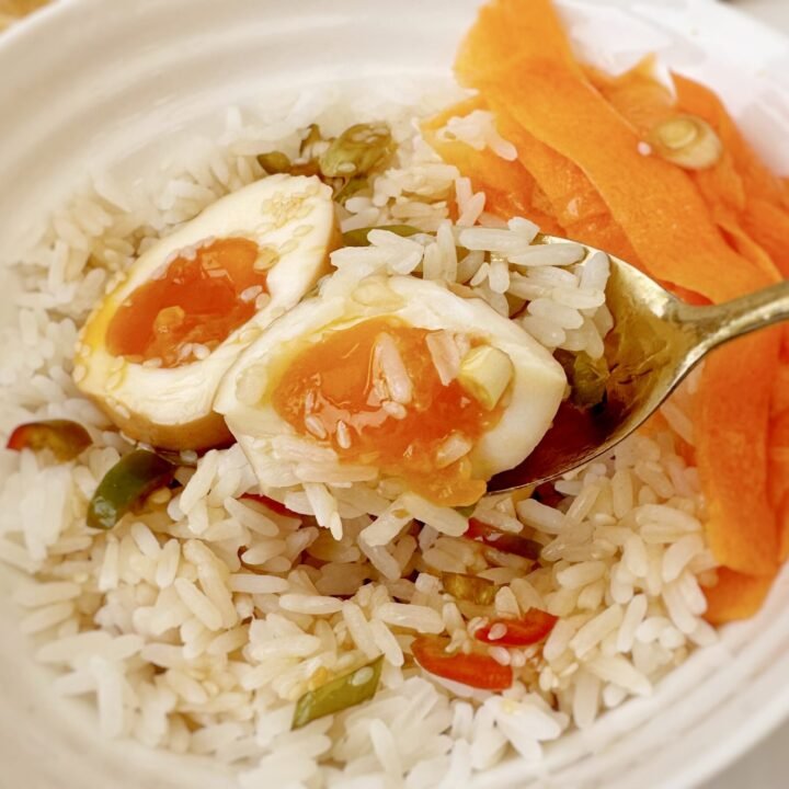 Jammy Korean Mayak Eggs halved on a plate, soaked in soy‑garlic marinade with sesame seeds, green onions and sliced chilli pepper.