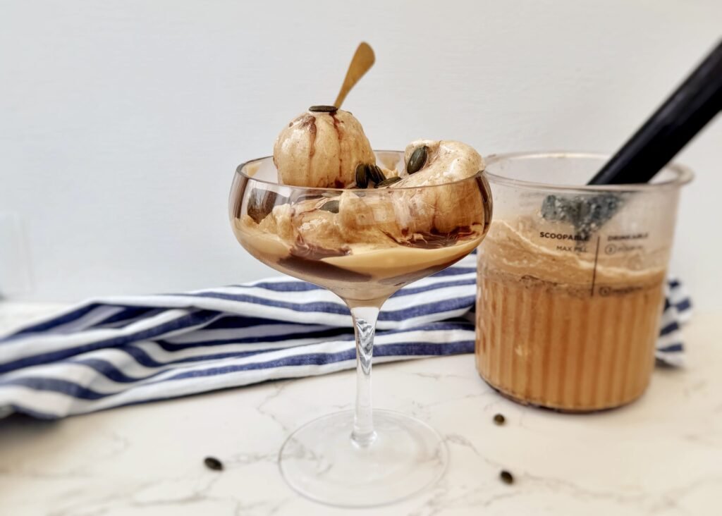 A scoop of creamy Latte Ice Cream in a bowl, topped with chocolate drizzle and coffee beans on a rustic background.