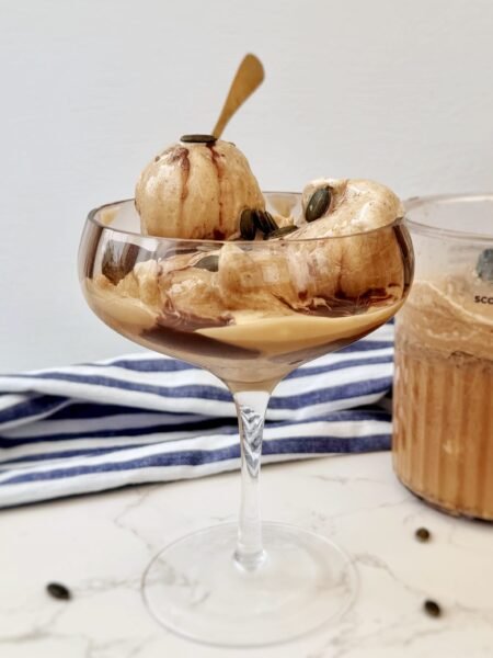 A scoop of creamy Latte Ice Cream in a bowl, topped with chocolate drizzle and coffee beans on a rustic background.