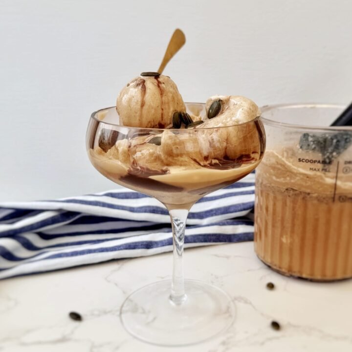 A scoop of creamy Latte Ice Cream in a bowl, topped with chocolate drizzle and coffee beans on a rustic background.