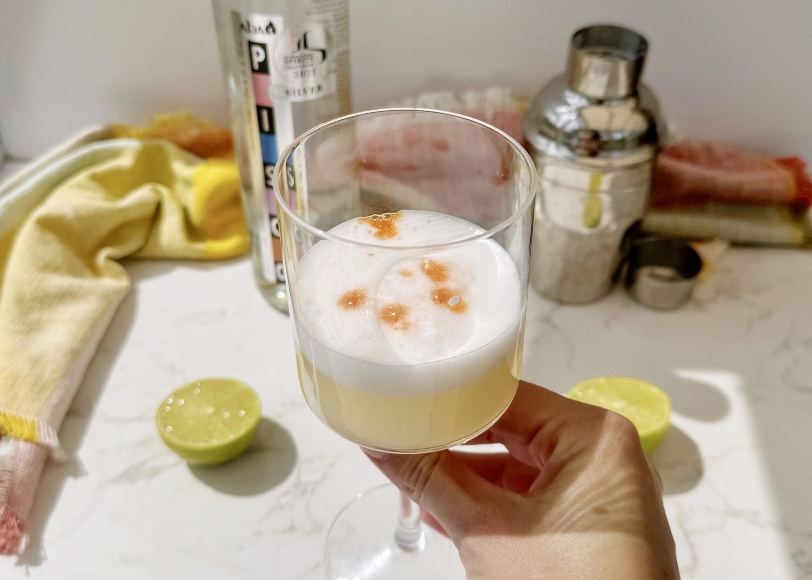 A frothy Pisco Sour cocktail in a chilled coupé glass, garnished with swirls of Angostura bitters on a creamy foam top, served with a lime wheel.