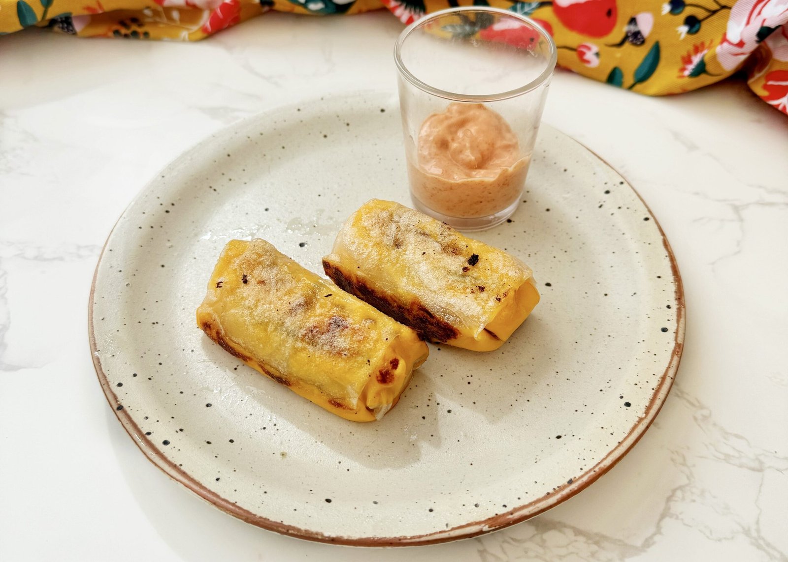 Crispy rice paper cheeseburger rolls filled with melted cheese, ground beef and pickles, served with dipping sauces on a platter.