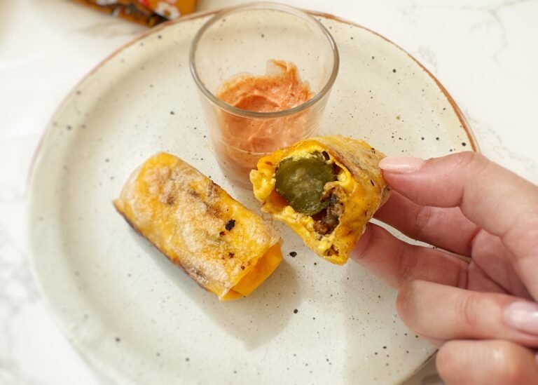 Crispy rice paper cheeseburger rolls filled with melted cheese, ground beef and pickles, served with dipping sauces on a platter.