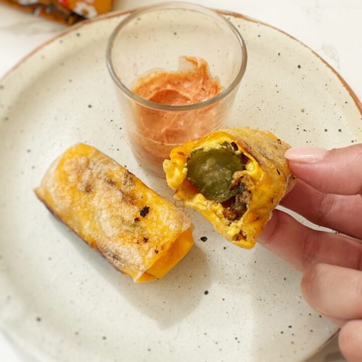 Crispy rice paper cheeseburger rolls filled with melted cheese, ground beef and pickles, served with dipping sauces on a platter.