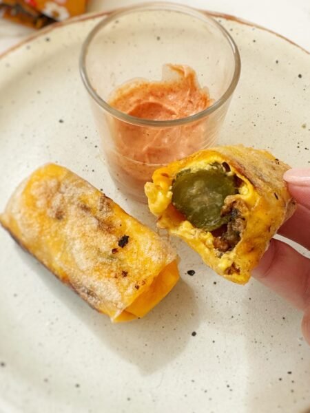 Crispy rice paper cheeseburger rolls filled with melted cheese, ground beef and pickles, served with dipping sauces on a platter.