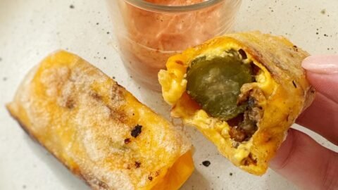 Crispy rice paper cheeseburger rolls filled with melted cheese, ground beef and pickles, served with dipping sauces on a platter.