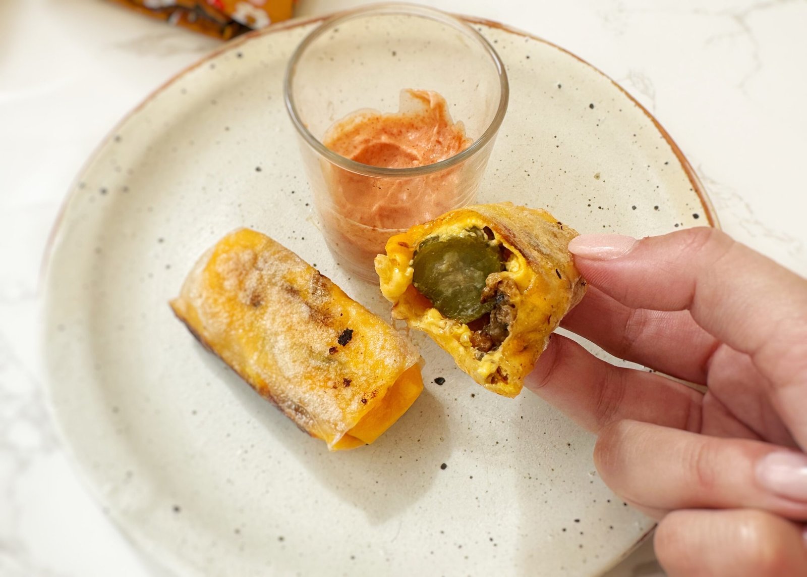 Crispy rice paper cheeseburger rolls filled with melted cheese, ground beef and pickles, served with dipping sauces on a platter.