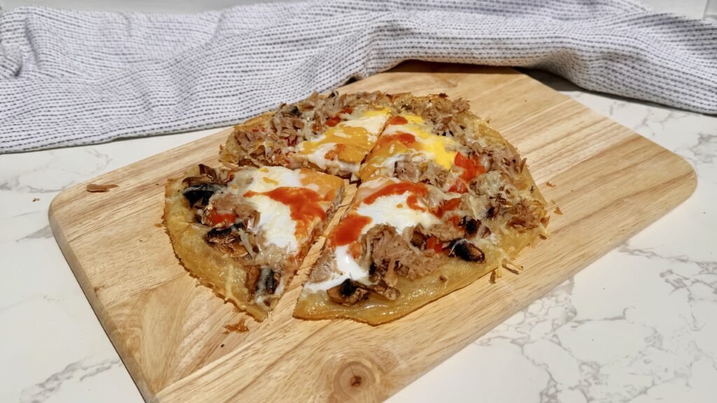 Chopping board showing a pizza made with rice paper and topped with peppers, tuna and egg