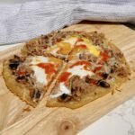 Chopping board showing a pizza made with rice paper and topped with peppers, tuna and egg