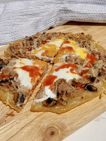 Chopping board showing a pizza made with rice paper and topped with peppers, tuna and egg