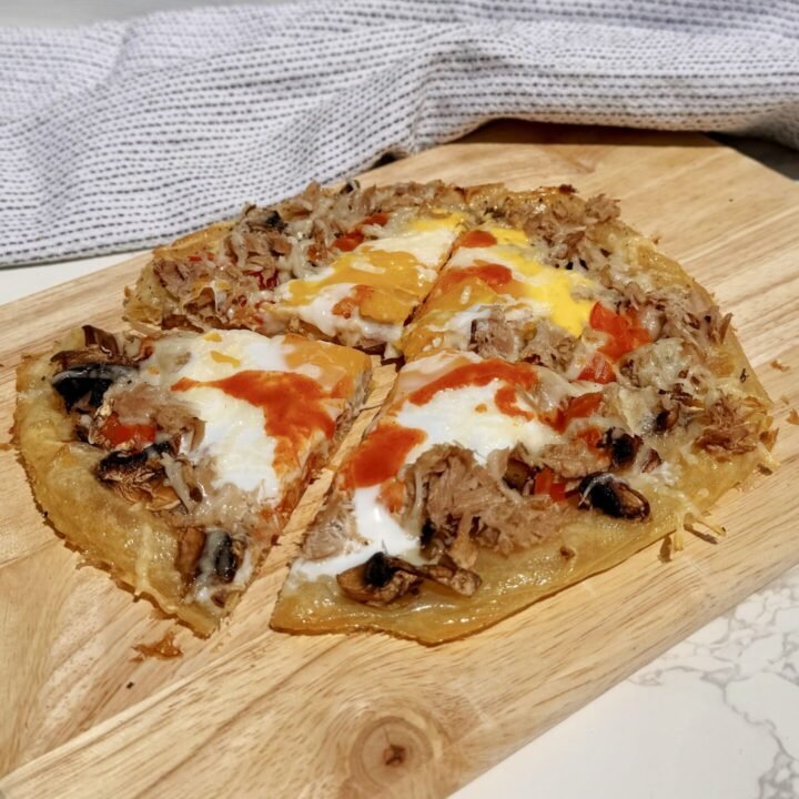 Chopping board showing a pizza made with rice paper and topped with peppers, tuna and egg