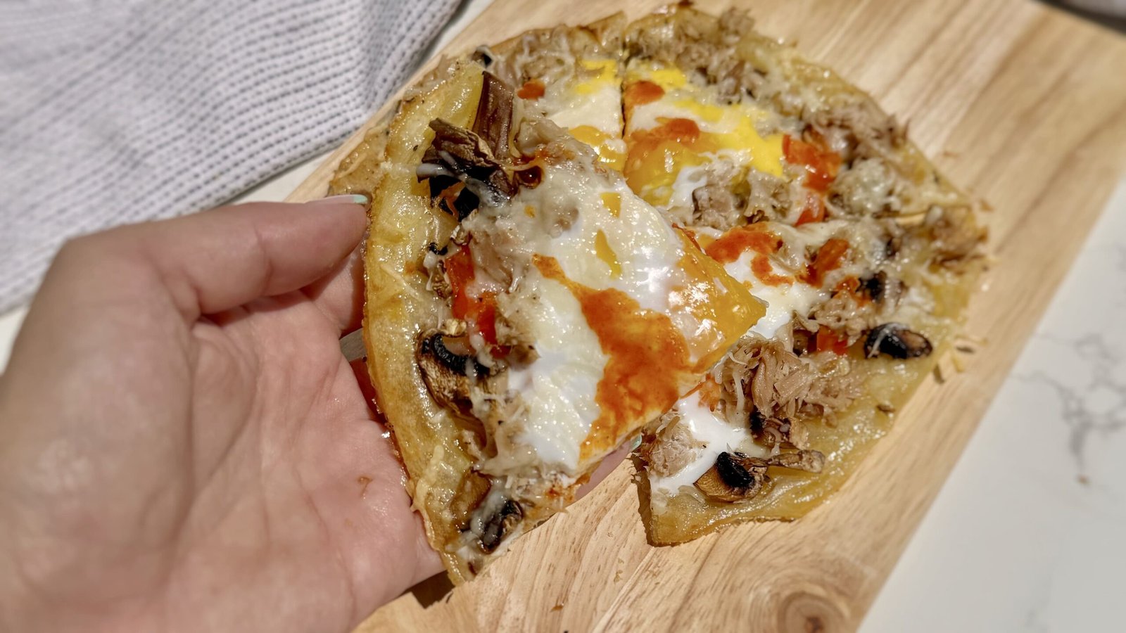 A hand holding a rice paper egg pizza topped with cheese and egg