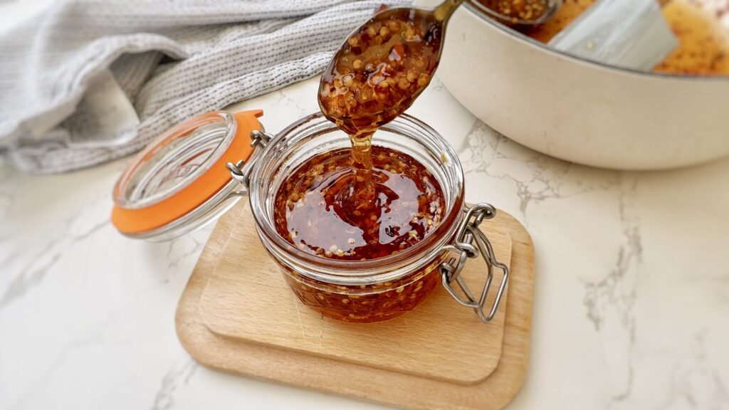 Glass Jar containing Homemade Hot Honey with chilli flakes with a spoon drizzling