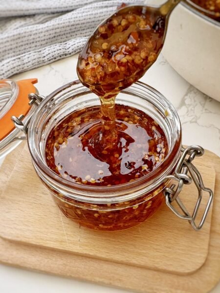 Glass Jar containing Homemade Hot Honey with chilli flakes with a spoon drizzling
