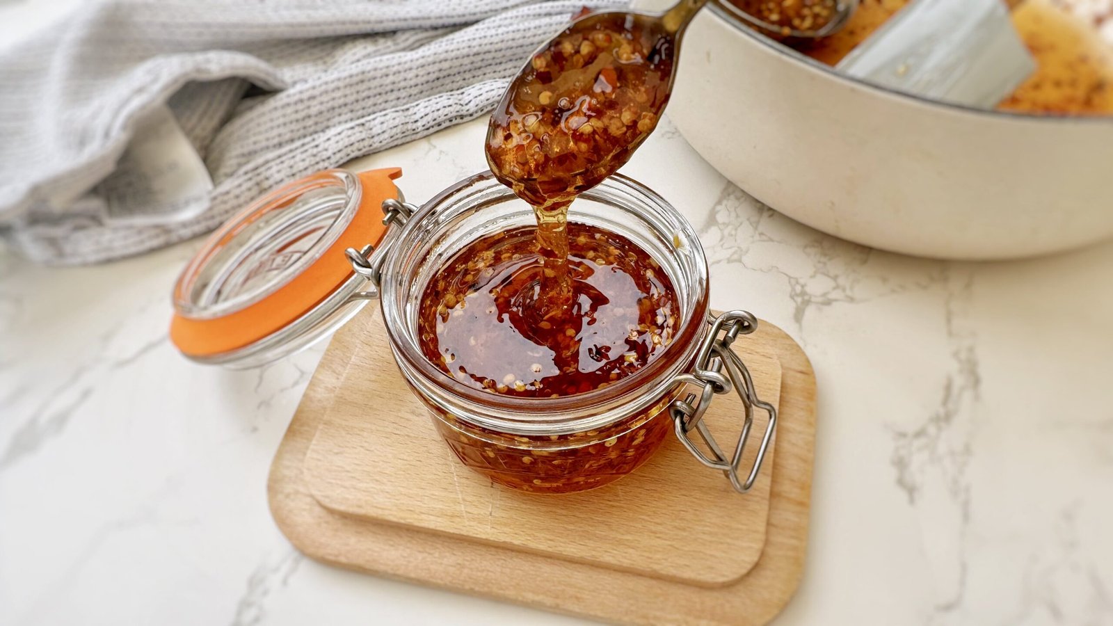 Glass Jar containing Homemade Hot Honey with chilli flakes with a spoon drizzling