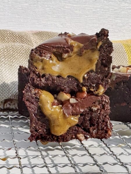 Brownie cup made with dates and nuts, filled with pistachio butter and topped with glossy dark chocolate, on a parchment-lined surface.