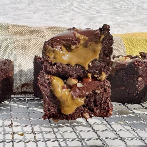 Brownie cup made with dates and nuts, filled with pistachio butter and topped with glossy dark chocolate, on a parchment-lined surface.