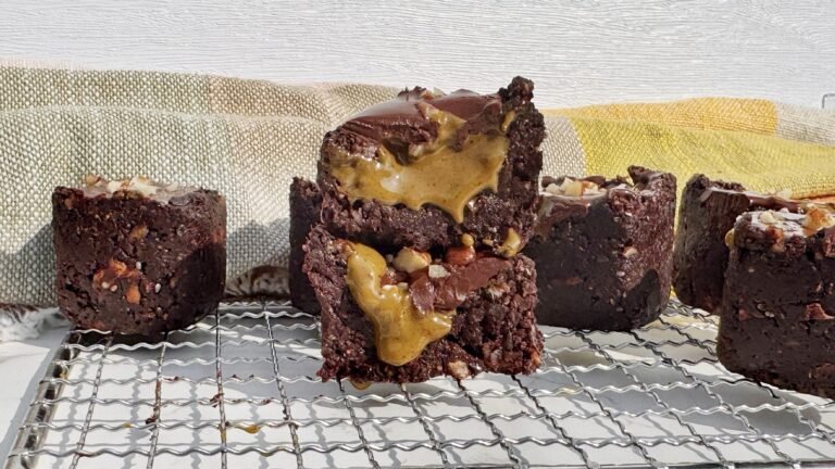 Brownie cup made with dates and nuts, filled with pistachio butter and topped with glossy dark chocolate, on a parchment-lined surface.