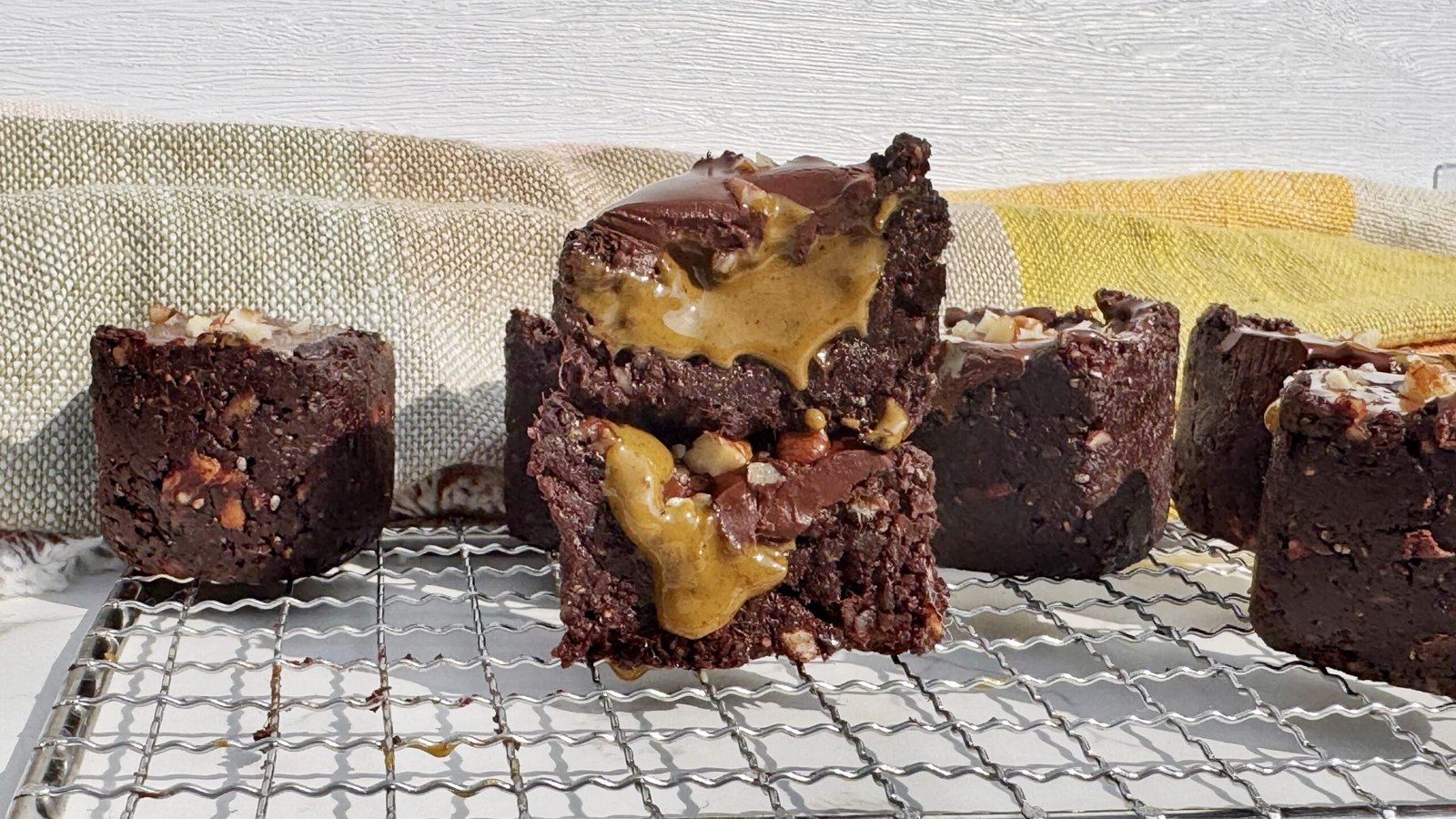 Brownie cup made with dates and nuts, filled with pistachio butter and topped with glossy dark chocolate, on a parchment-lined surface.