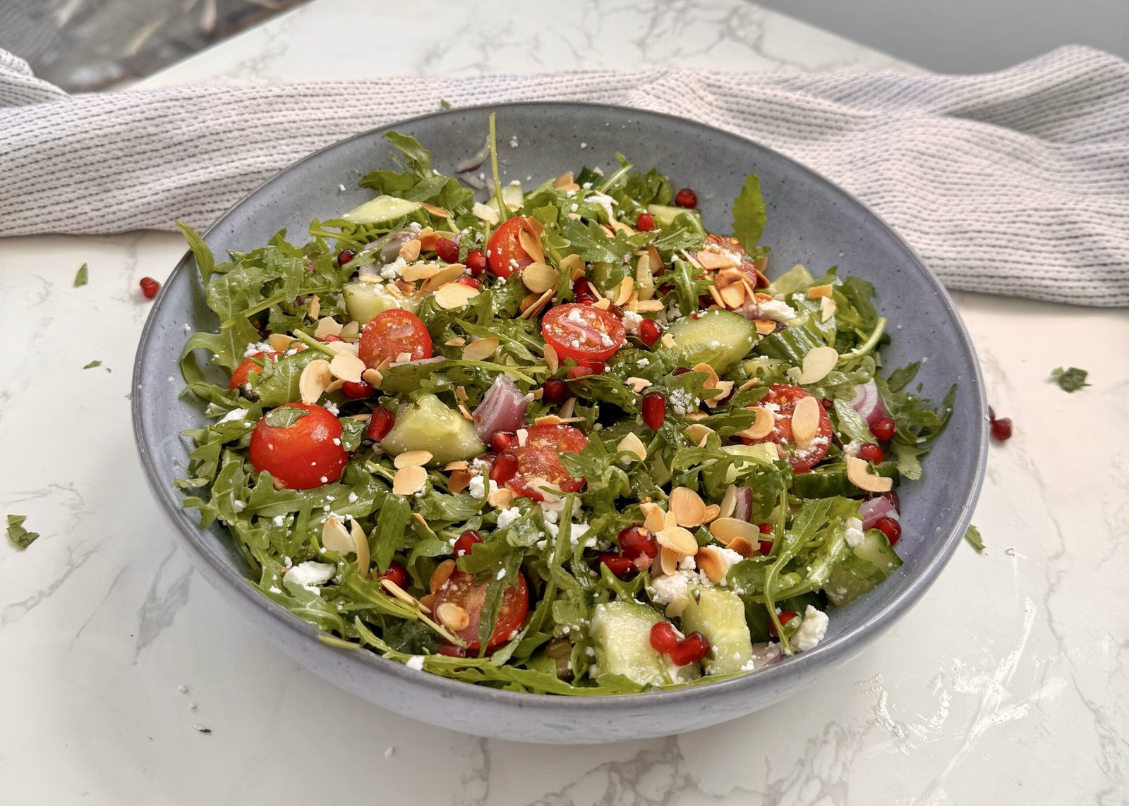 A fresh bowl of Arugula & Date Salad with arugula leaves, sliced Medjool dates, cherry tomatoes, feta, and toasted almonds drizzled with lemon-honey dressing.