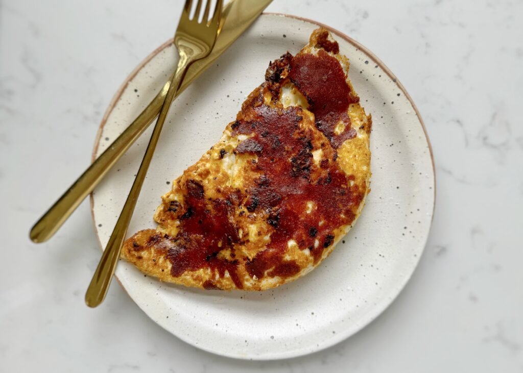 Close-up of crispy mozzarella and red pesto eggs in a frying pan, with golden cheese edges, vibrant red pesto base, and perfectly cooked sunny-side-up eggs. Preguntar a ChatGPT
